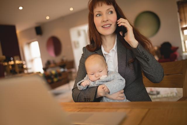 Mother talking on mobile phone while holding her baby - Download Free Stock Photos Pikwizard.com