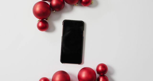 Image of red christmas baubles and smartphone on white background. christmas, tradition and celebration concept.