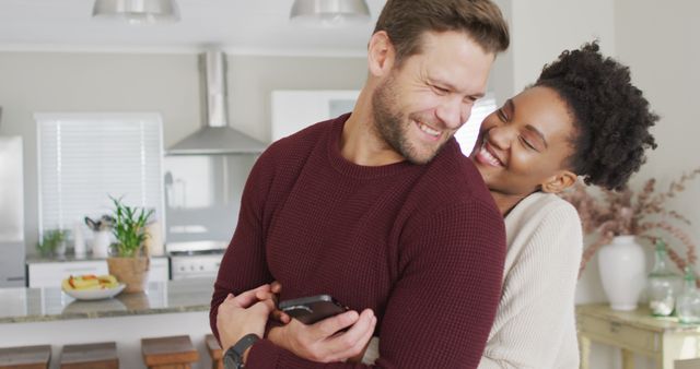 Image of happy diverse couple hugging and using smartphone in kitchen - Download Free Stock Photos Pikwizard.com