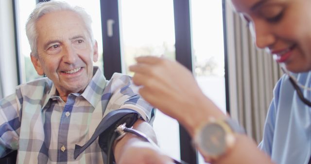 Image of happy biracial female doctor checking pressure to caucasian senior man. seniors health and nursing home lifestyle concept digitally generated image.