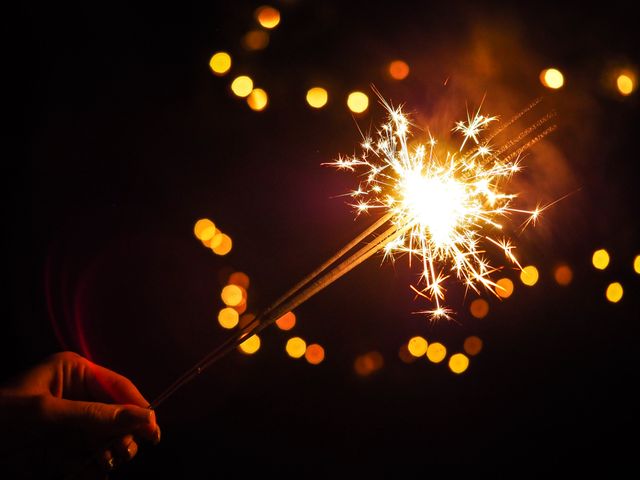 Hand holding a burning sparkler against dark background. Celebration and festivity concept