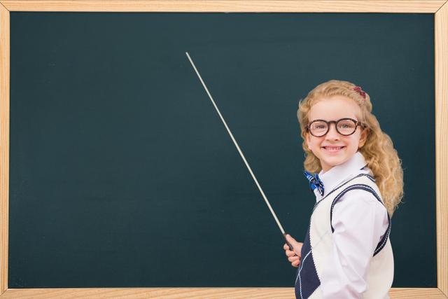 Side view of smiling schoolgirl with stick standing by blackboard - Download Free Stock Photos Pikwizard.com
