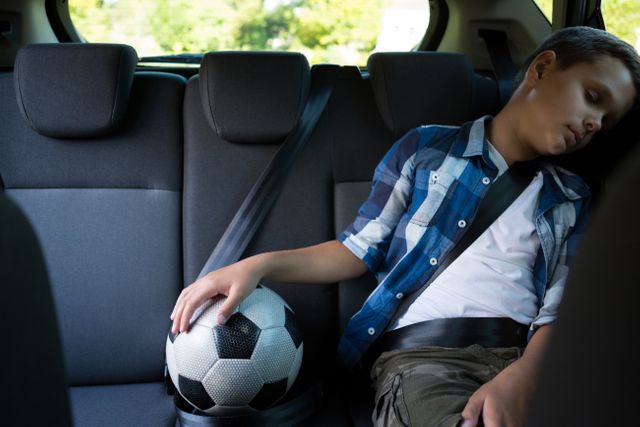 Teenage boy sitting with football in the back seat of car