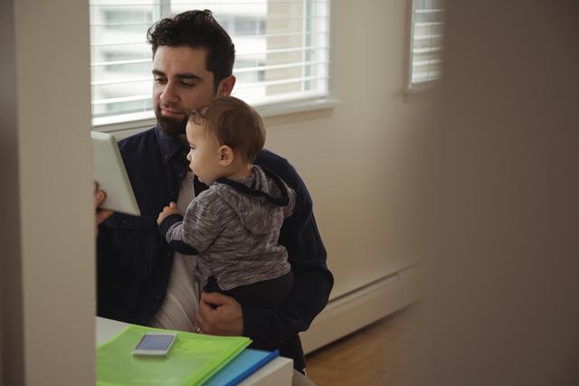 Father holding his baby while using digital tablet at desk - Download Free Stock Photos Pikwizard.com