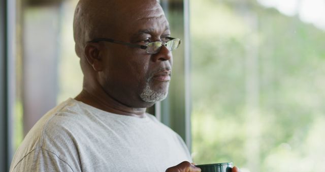 Thoughtful african american senior man drinking mug of coffee and smiling. retirement lifestyle, spending time alone at home.