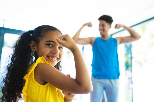 Portrait of happy hispanic girl flexing muscles against father at home - Download Free Stock Photos Pikwizard.com