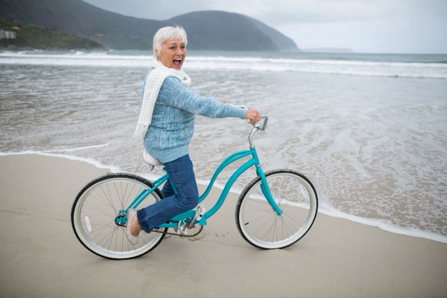 Senior woman riding bicycle on the beach - Download Free Stock Photos Pikwizard.com