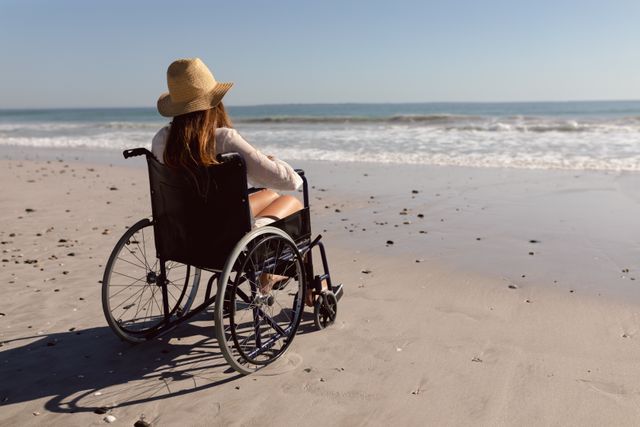 Disabled woman in hat sitting on wheelchair at beach in the sunshine - Download Free Stock Photos Pikwizard.com