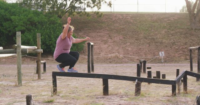 Happy plus size caucasian woman balancing on beam at bootcamp training course. Female fitness, challenge and healthy lifestyle.