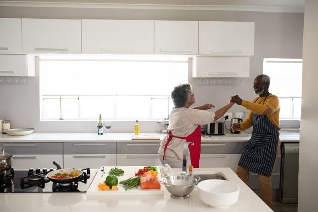 Senior couple in apron dancing together in the kitchen - Download Free Stock Photos Pikwizard.com