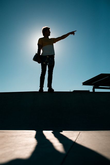 Silhouette of caucasian man holding skateboard, standing, pointing something - Download Free Stock Photos Pikwizard.com