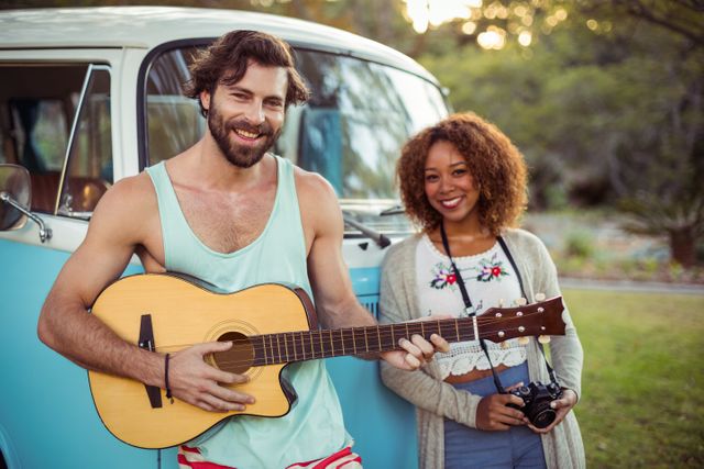 Man playing guitar near campervan while woman standing beside him - Download Free Stock Photos Pikwizard.com