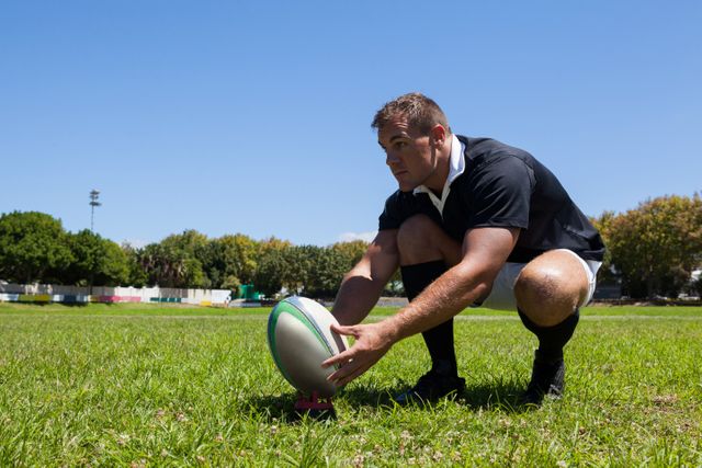 Rugby player holding ball while kneeling on grass - Download Free Stock Photos Pikwizard.com