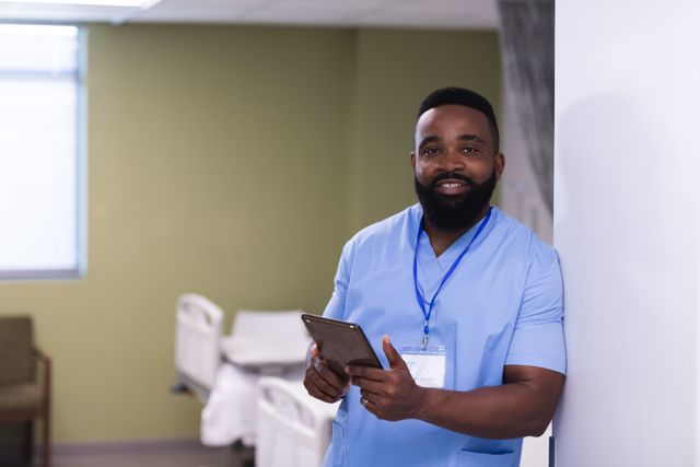 Portrait of smiling, bearded african american male doctor using tablet in hospital ward, copy space. Medical services, hospital and healthcare concept.