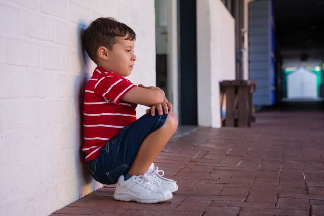 Side view of boy crouching by wall - Download Free Stock Photos Pikwizard.com