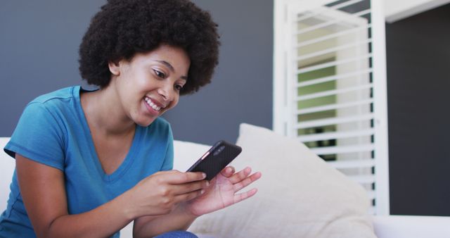 African american woman using smartphone while sitting on the couch at home. staying at home in self isolation in quarantine lockdown