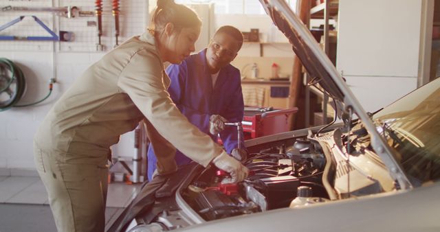 Image of two diverse female car mechanics talking and repairing car. working in car repair shop and running small feminine business concept.