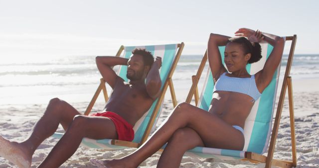 African american couple sunbathing while sitting on deck chairs at the beach - Download Free Stock Photos Pikwizard.com