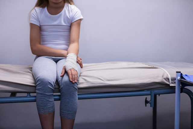 Girl with injured hand sitting on stretcher bed - Download Free Stock Photos Pikwizard.com