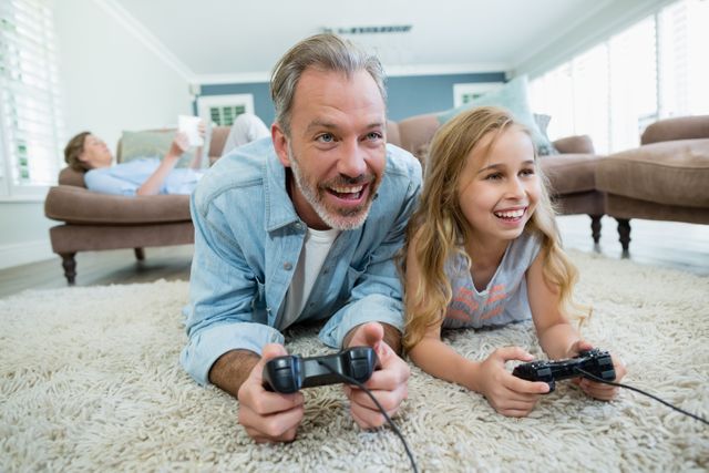 Happy father and daughter playing video game while lying on floor at home