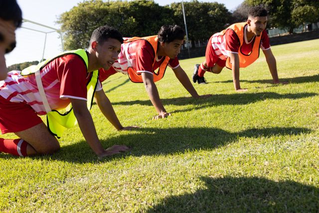 Multiracial soccer team players wearing red jersey and sports bibs doing push-ups on grassy land - Download Free Stock Photos Pikwizard.com
