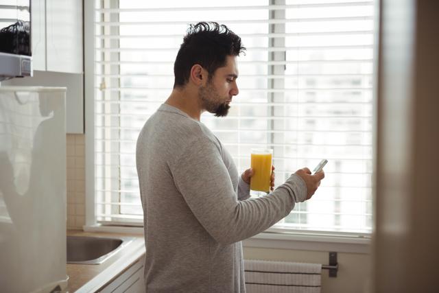 Man using mobile phone while having juice in kitchen at home