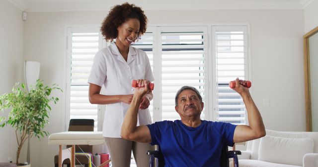 Mixed race female physiotherapist helping senior man exercise using dumbbells. senior healthcare physiotherapy home visit.