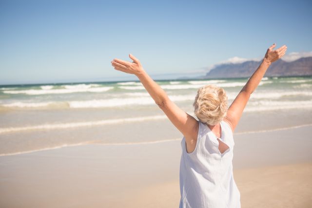 Rear view of woman with arms raised standing on shore - Download Free Stock Photos Pikwizard.com