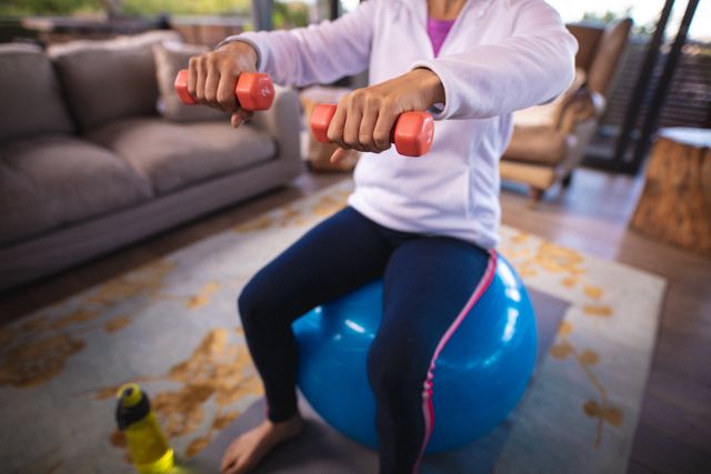 Portrait of smiling senior caucasian woman sitting on swiss ball, exercising with dumbbells. retirement lifestyle, spending time alone at home.