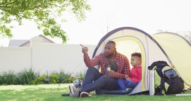 Happy african american father and his son sitting in tent in garden. Spending quality time at home.