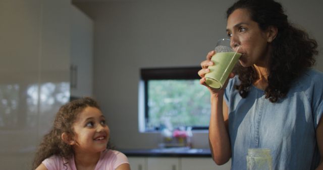 Mixed race mother and daughter drinking smoothie in the kitchen. domestic life and family leisure time concept.