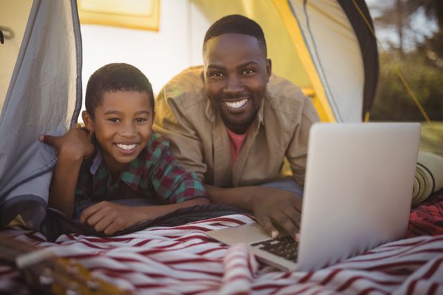 Smiling father and son using laptop in tent - Download Free Stock Photos Pikwizard.com