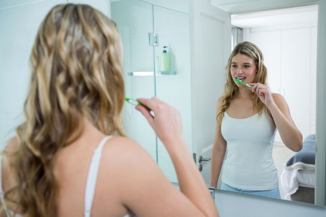 Woman looking in mirror while brushing her teeth in bathroom - Download Free Stock Photos Pikwizard.com