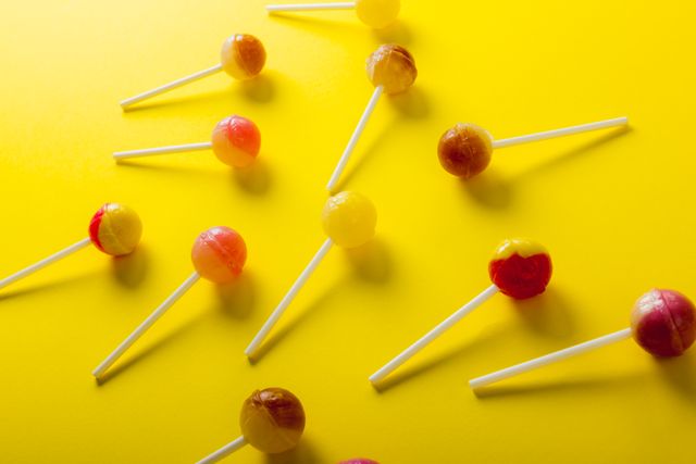 Overhead view of sweet lollipops scattered against yellow background. unaltered, unhealthy eating and sweet food concept.
