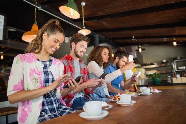 Friends using their mobile phones while sitting by coffee cups on table in restaurant