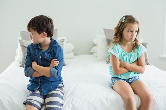 Sad siblings sitting with arms crossed in bedroom at home