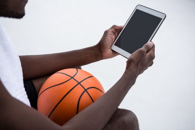 Player holding basketball while using digital tablet on terrace