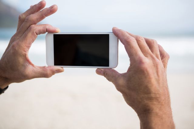 Close-up of mans hand taking picture on mobile phone on beach - Download Free Stock Photos Pikwizard.com
