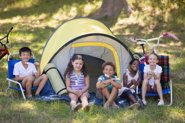 Portrait of cheerful children sitting outside tent at campsite