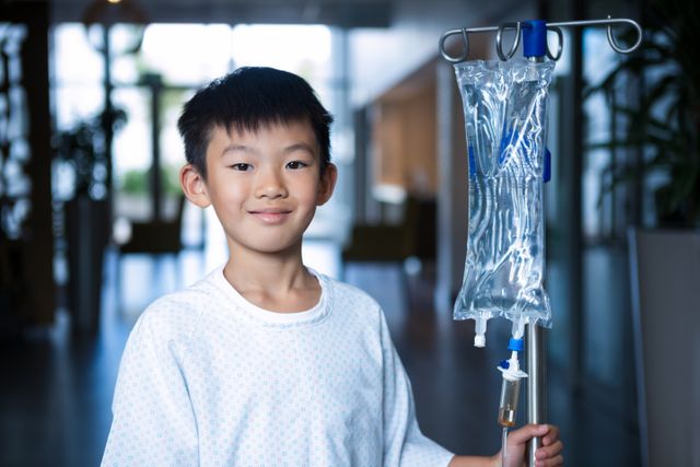 Smiling boy patient holding intravenous iv drip stand in corridor - Download Free Stock Photos Pikwizard.com