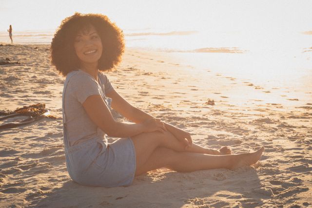Happy african american woman sitting on beach and relaxing during sunset - Download Free Stock Photos Pikwizard.com