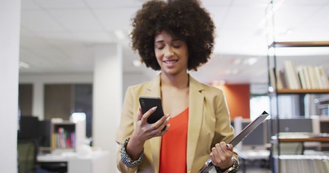 Image of biracial businesswoman walking and using smartphone in office. business professionals and working in office concept.