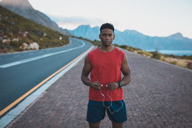 Fit african american man exercising outdoors on coastal road holding headphones - Download Free Stock Photos Pikwizard.com