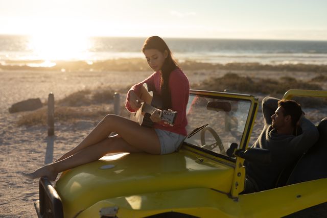 Happy caucasian couple with beach buggy on beach at sunset, woman sitting on car playing guitar - Download Free Stock Photos Pikwizard.com