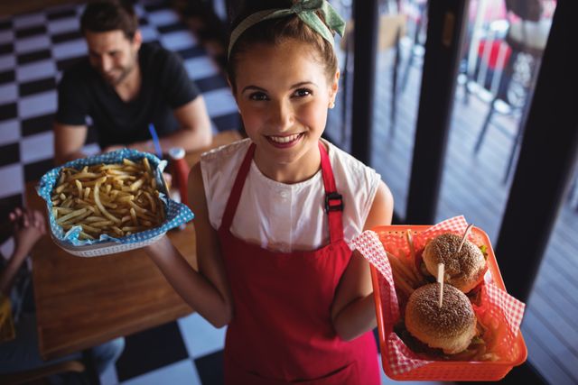 Portrait of a waitress holding burger and french fries in tray at restaurant