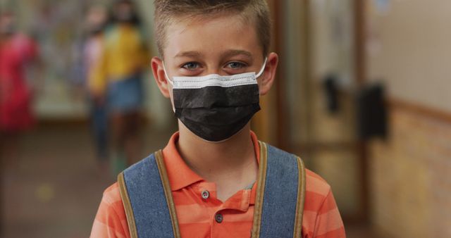 Portrait of caucasian schoolboy wearing face mask, standing in corridor looking at camera. children in primary school during coronavirus covid 19 pandemic.