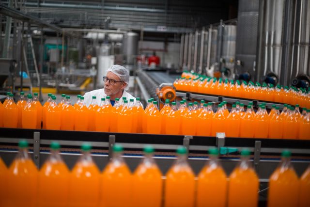 Factory engineer monitoring filled juice bottle on production line - Download Free Stock Photos Pikwizard.com