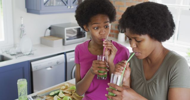 Happy african american mother and daughter drinking healthy drink in kitchen. domestic life and quality family time together at home.