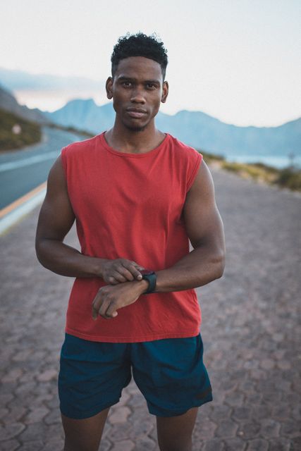 Fit african american man exercising outdoors on coastal road checking smartwatch - Download Free Stock Photos Pikwizard.com