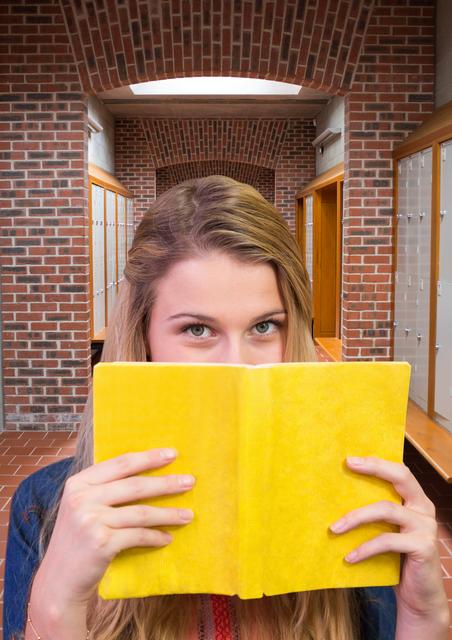 Teenage student hiding her face behind book in locker room - Download Free Stock Photos Pikwizard.com